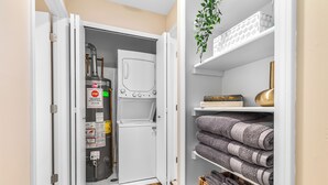 A laundry room with a washing machine, a water heater, and towels stored on shelves.