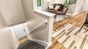 A staircase with a handrail, a wooden floor, a beige wall, a white door, and a brown leather sofa with a white pillow.