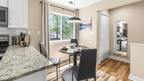 A modern kitchen with a granite countertop, a dining area with a round table and chairs, and a view of the outdoors through large windows.