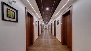 A long, narrow hallway with wooden doors on both sides, a wooden floor, and recessed lighting on the ceiling. - Grand Fortune Beacon Ichalkaranji (Hatkalangda)