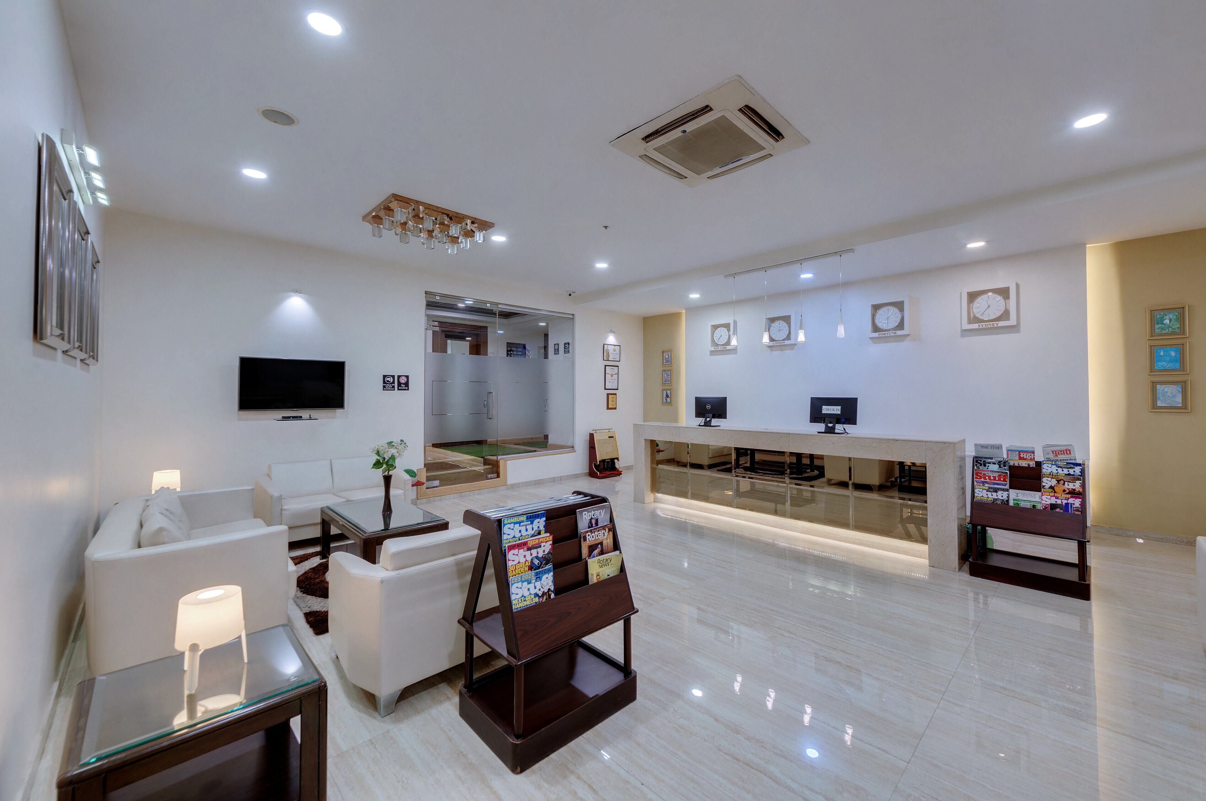 A modern hotel lobby with a reception desk, seating area, and a TV mounted on the wall.