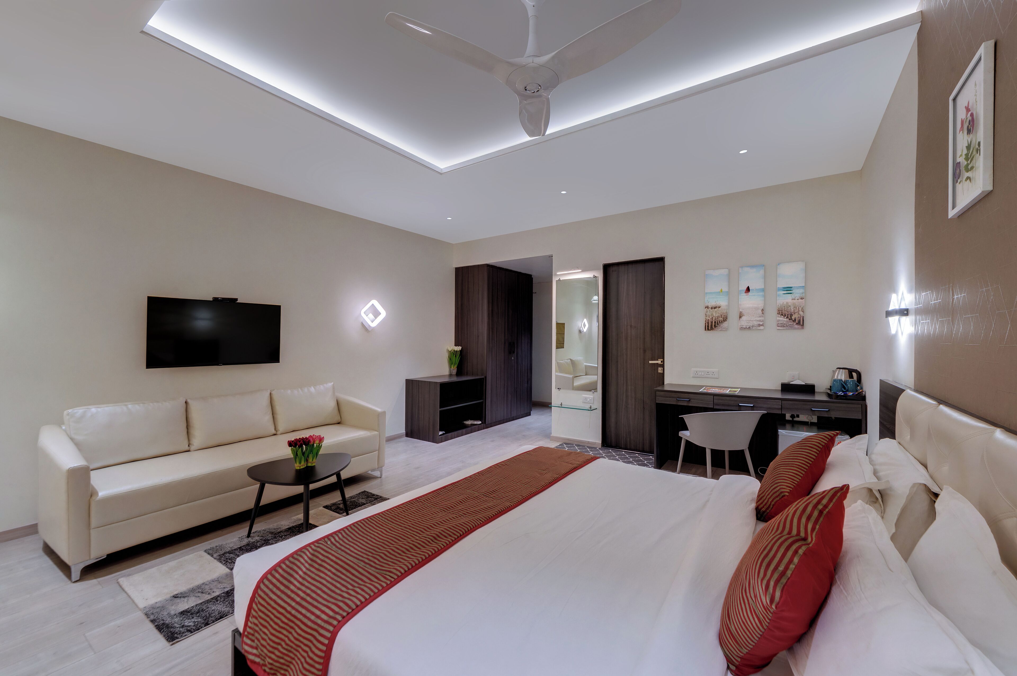 A modern hotel room with a large bed, a sofa, a desk, and a TV.