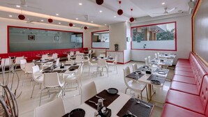 A modern restaurant with white and red decor, multiple dining tables, and a large mirror. - Grand Fortune Beacon Ichalkaranji (Hatkalangda)