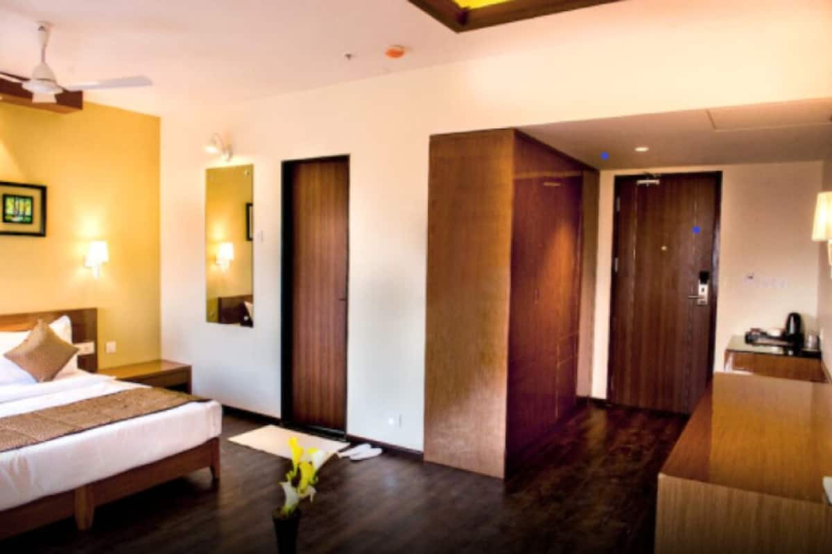 A hotel room with a bed, bedside table, lamp, and a large mirror.