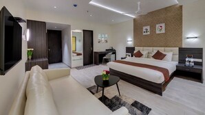 A modern hotel room with a large bed, a desk, a sofa, and a small table with a vase of flowers. - Grand Fortune Beacon Ichalkaranji (Hatkalangda)