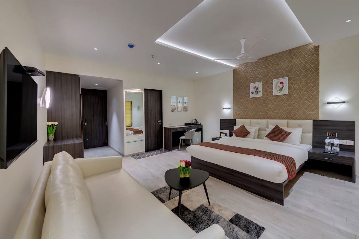 A modern hotel room with a large bed, a desk, a sofa, and a small table with a vase of flowers.