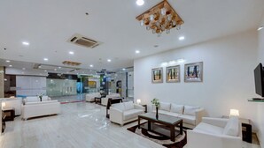 A modern hotel lobby with white sofas, a coffee table, and a chandelier. - Grand Fortune Beacon Ichalkaranji (Hatkalangda)