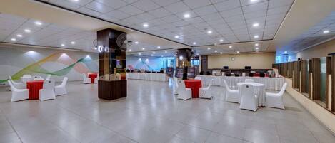 A spacious indoor venue with multiple round tables and white chairs, a central reception area, and a large wall mural.