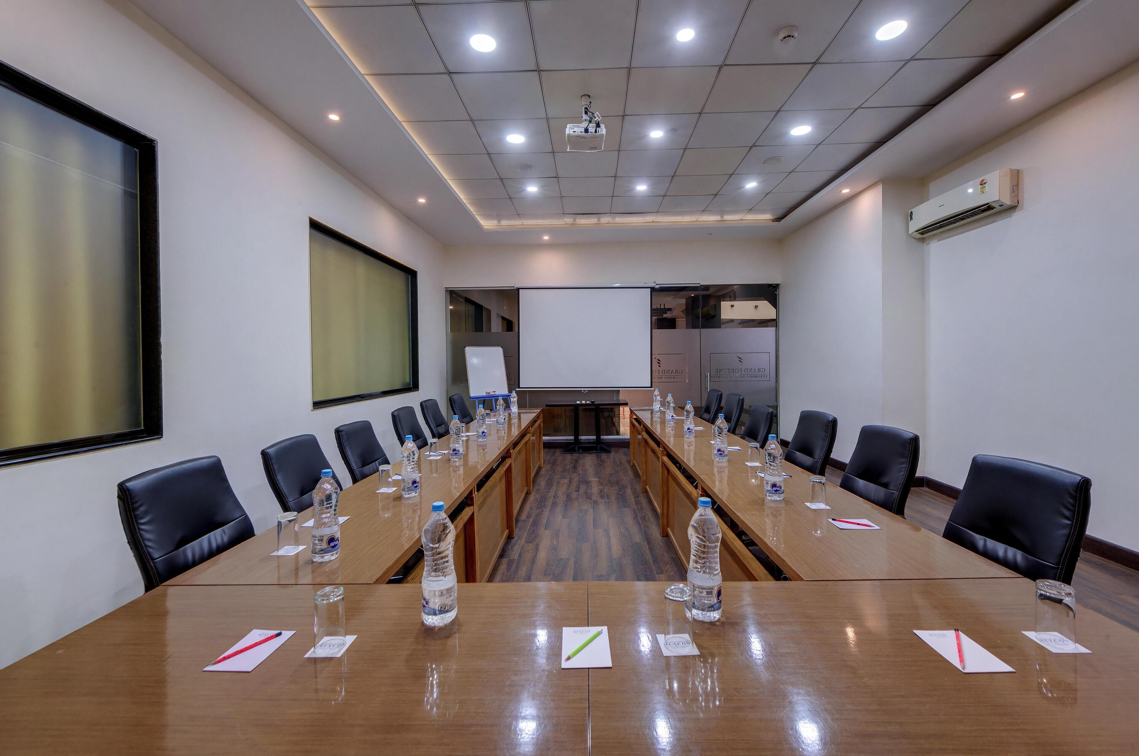 A conference room with a long table, black chairs, water bottles, name cards, and a projector screen.