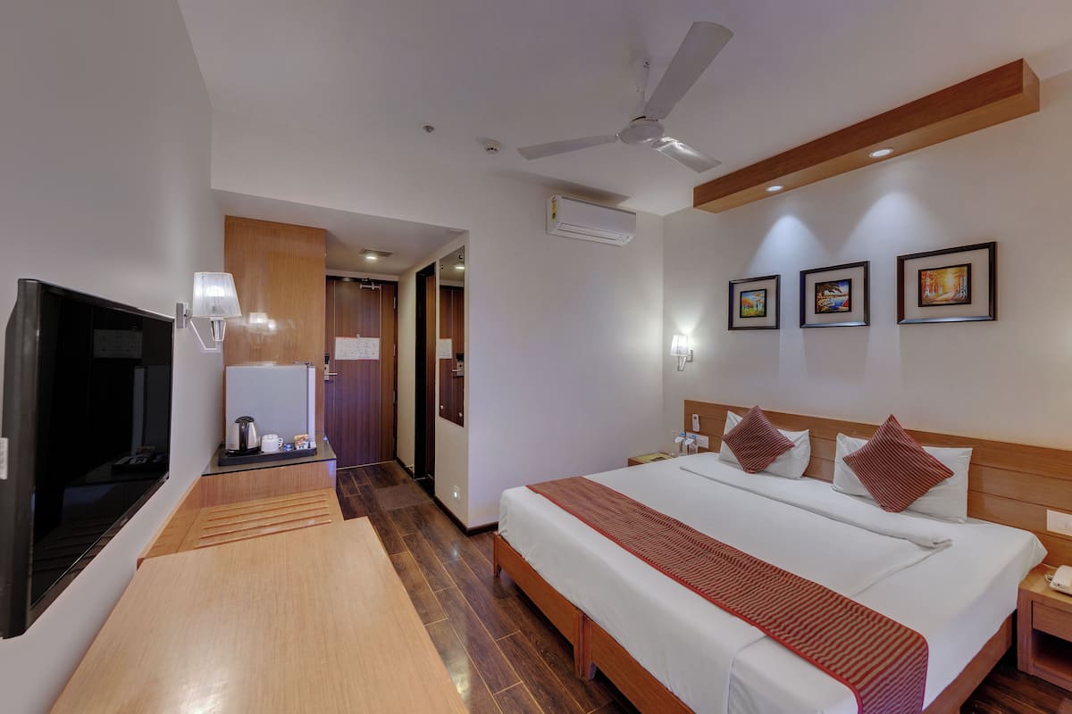 A hotel room with a bed, bedside table, TV, and a wooden floor.