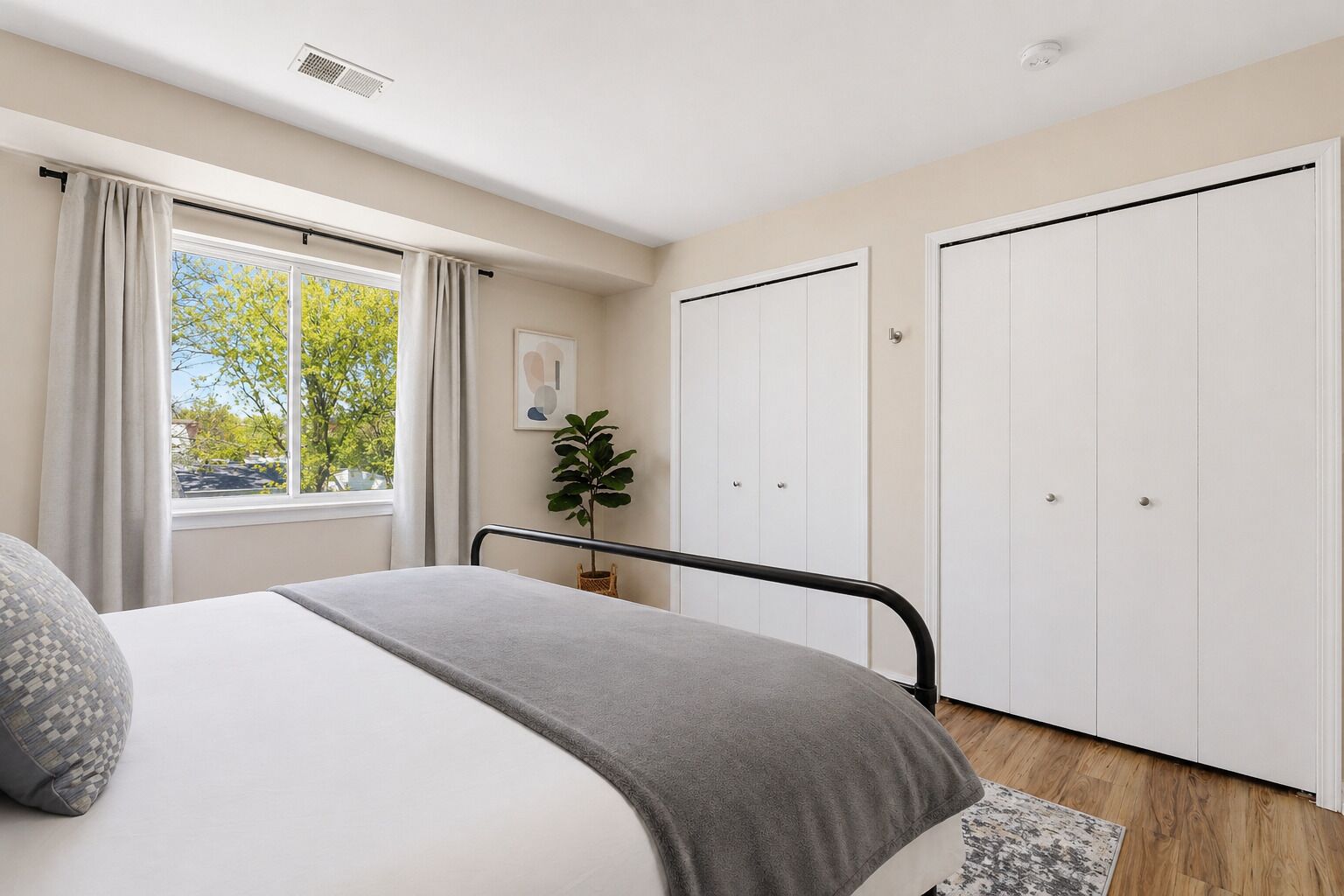 Une chambre à coucher avec un lit, une fenêtre avec des rideaux, une plante et une armoire.