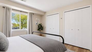 Une chambre à coucher avec un lit, une fenêtre avec des rideaux, une plante et une armoire.