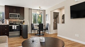 Una cocina moderna con armarios oscuros, electrodomésticos de acero inoxidable y un comedor con una mesa redonda y sillas.