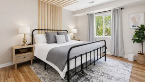 Un dormitorio con cama, mesitas de noche, una ventana con cortinas, una planta y una lámpara en el techo.