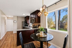 A modern kitchen with dark wood cabinets, stainless steel appliances, and a large window offering a view of trees.