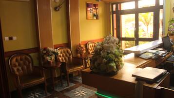 A reception area with a wooden desk, chairs, a vase of flowers, and a window with a view of greenery.