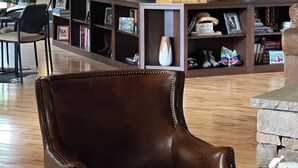 Una stanza con soffitto in legno, una poltrona in pelle marrone, una libreria in legno e teste di animali appese al muro.