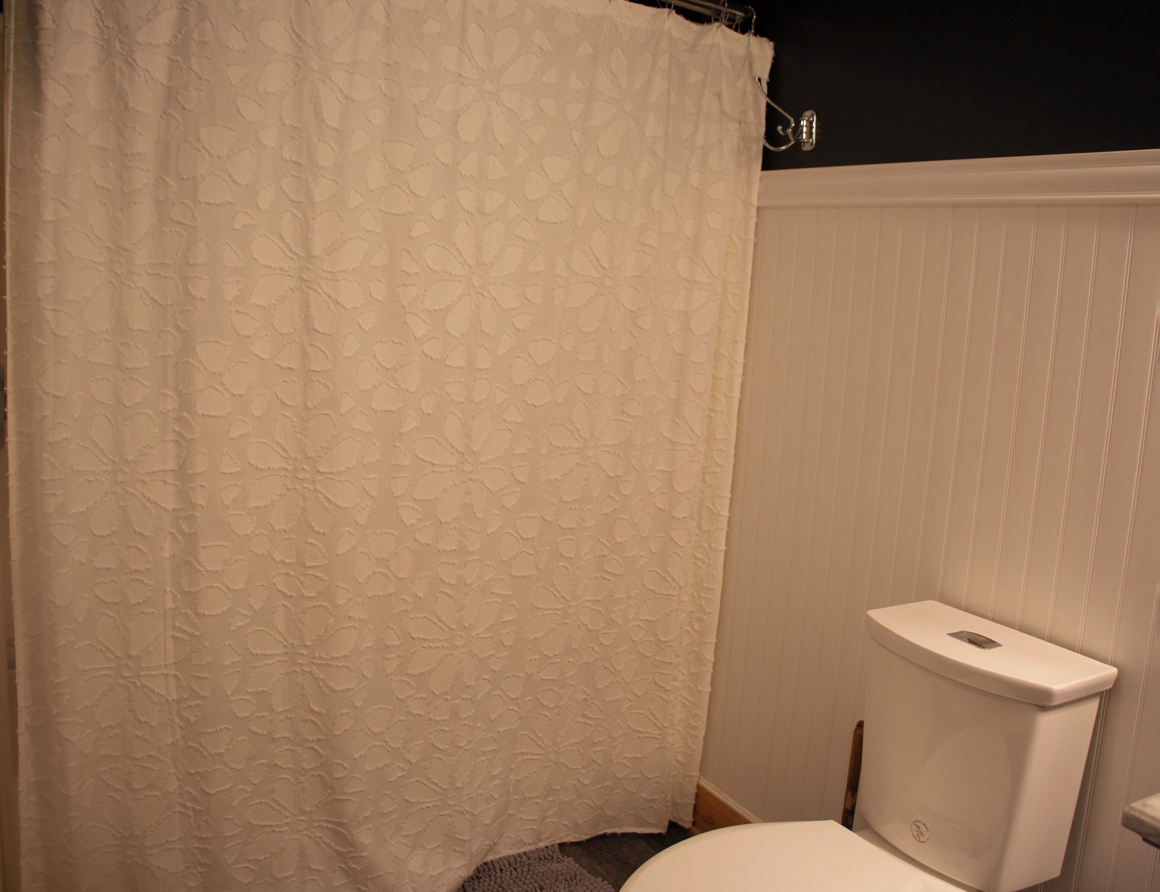 Un baño con inodoro, cortina de ducha y radiador, todo en color blanco.