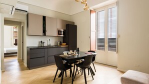 A modern kitchen with dark cabinetry, a dining table with chairs, and a large window with blinds.