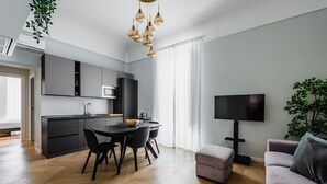 A modern kitchen with dark cabinets, a dining table with chairs, and a flat-screen TV mounted on the wall.