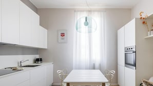 A modern kitchen with white cabinets, a dining table, and a sofa. - Crociali Apartment by Wonderful Italy (Bologna)