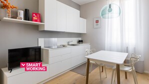A modern kitchen with white cabinetry, a flat-screen TV, and a dining area with a table and chairs. - Crociali Apartment by Wonderful Italy (Bologna)