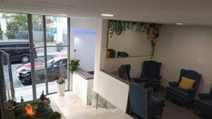 A reception area with a desk, chairs, and a view of parked cars through large windows. - Hostel Funchal XII (Funchal)