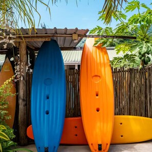 Three kayaks of different colors (blue, orange, and yellow) leaning against a wooden fence in an outdoor setting. - Mae Water Front Apartments (Mahé Island)