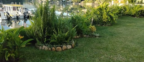 A serene lakeside garden with a wooden bench, lush greenery, and a boat docked by the water.