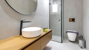 Une salle de bain moderne avec un miroir rond, un lavabo blanc et une douche à parois de verre.