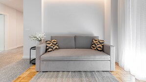 Un salon moderne avec un canapé gris, des coussins à motifs, une petite table d’appoint et un vase avec des fleurs blanches.