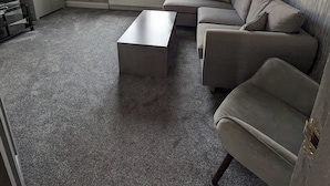 Een woonkamer met een bank, een bijzettafeltje en een raam met gordijnen.