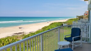 A balcony with a view of a beach, a chair, and a small table. - Unbelievable View- No other unit has a view like this one. (Indialantic)