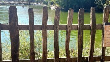 A wooden fence with a cat sitting on it, overlooking a body of water with a building in the background.