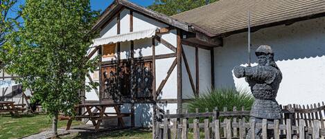 Un bâtiment traditionnel à la façade blanche et aux éléments en bois apparent, une statue de pierre devant et une table de pique-nique à proximité.
