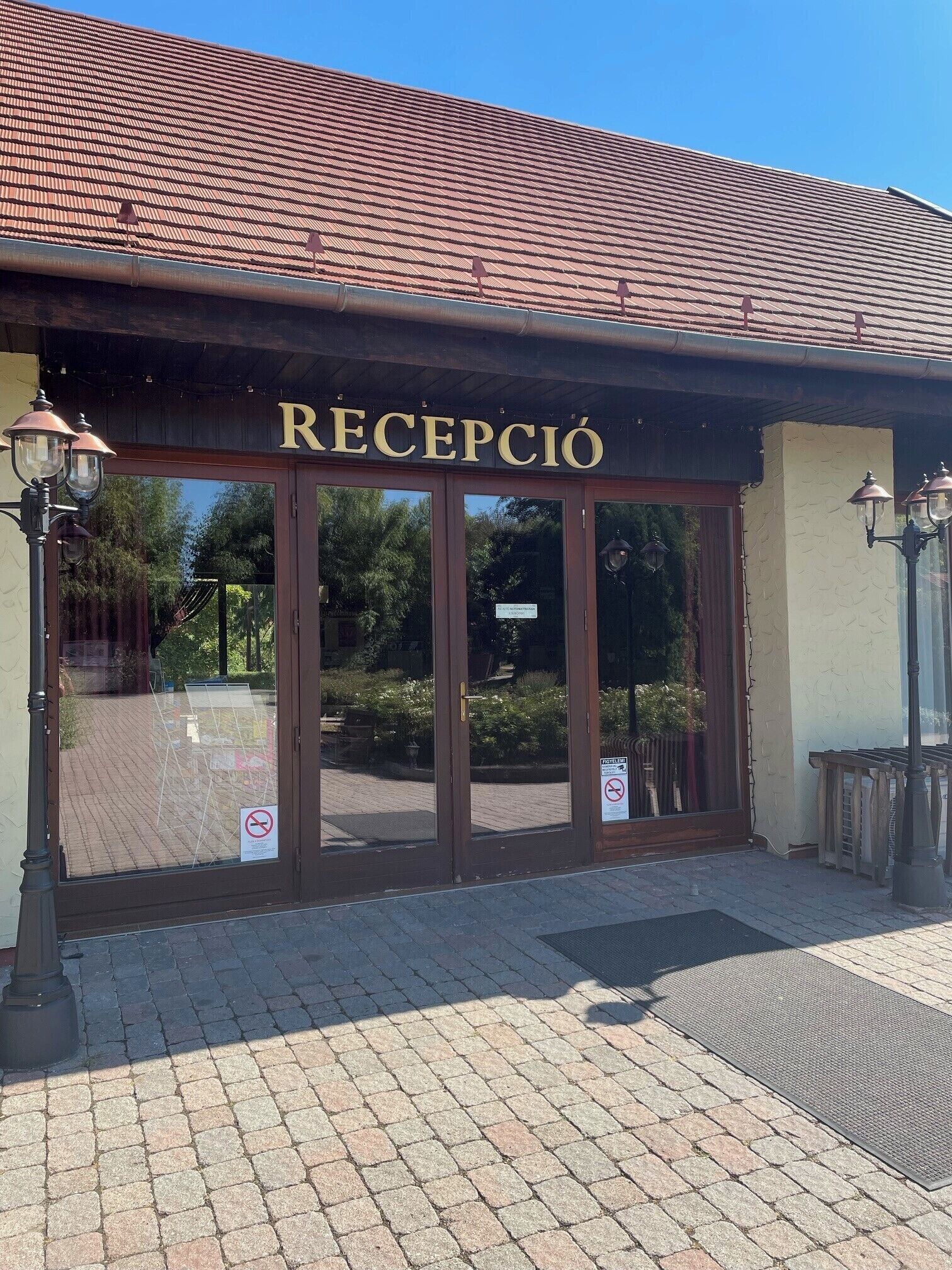 A building entrance with the sign "RECEPCIÓN" above the doors, a paved walkway, and a tiled roof.