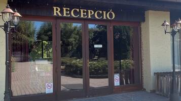 A building entrance with the sign "RECEPCIÓN" above the doors, a paved walkway, and a tiled roof.