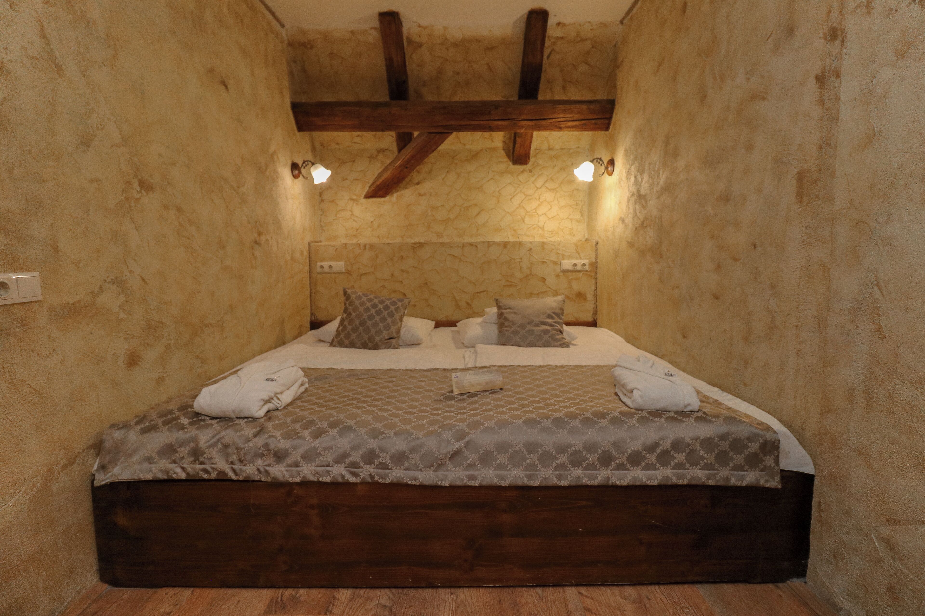A bedroom with a wooden headboard, a patterned bedspread, and two bedside lamps.