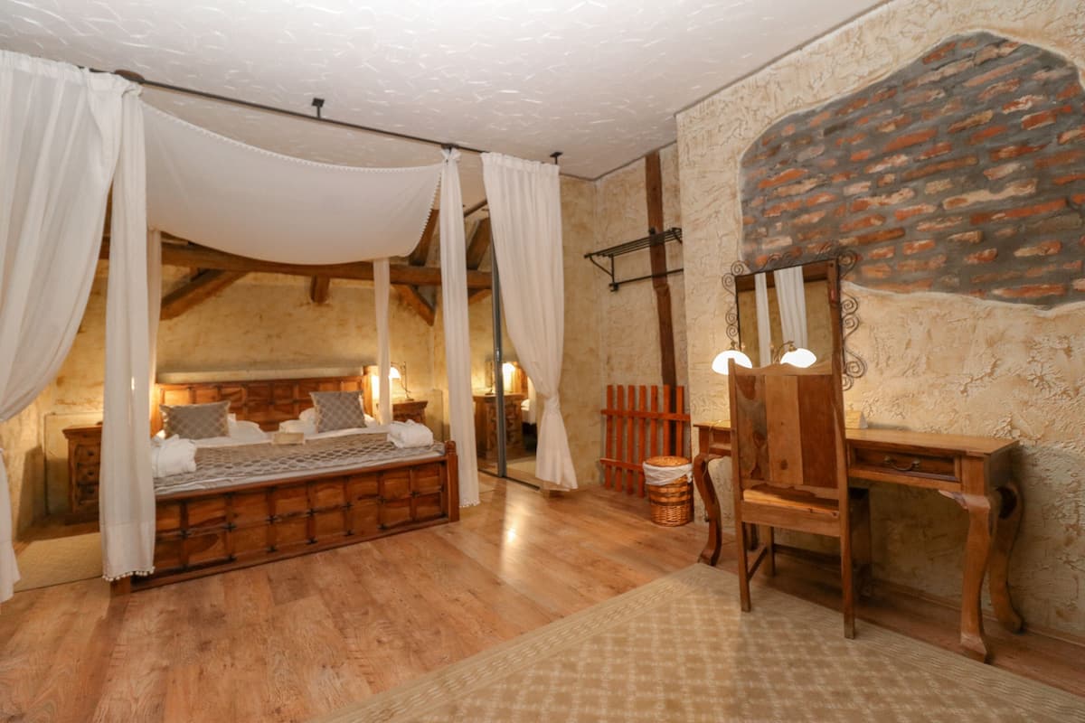 Un dormitorio rústico con cama de madera, cortinas blancas, un escritorio de madera y una pared de piedra.