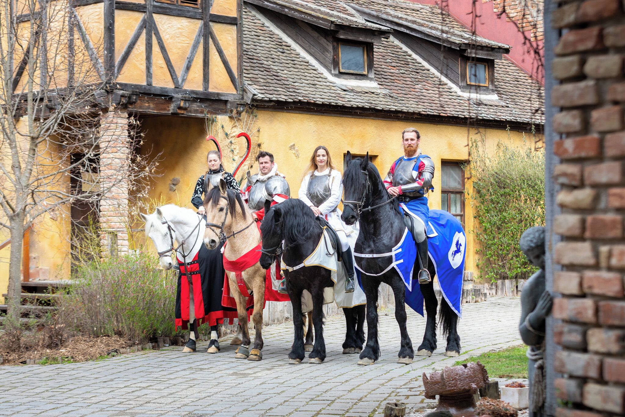 A medieval reenactment scene with people in armor and horses in front of a half-timbered building.