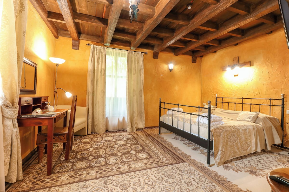 Un dormitorio con techo de madera, una cama con colcha estampada, un escritorio con lámpara y una silla.
