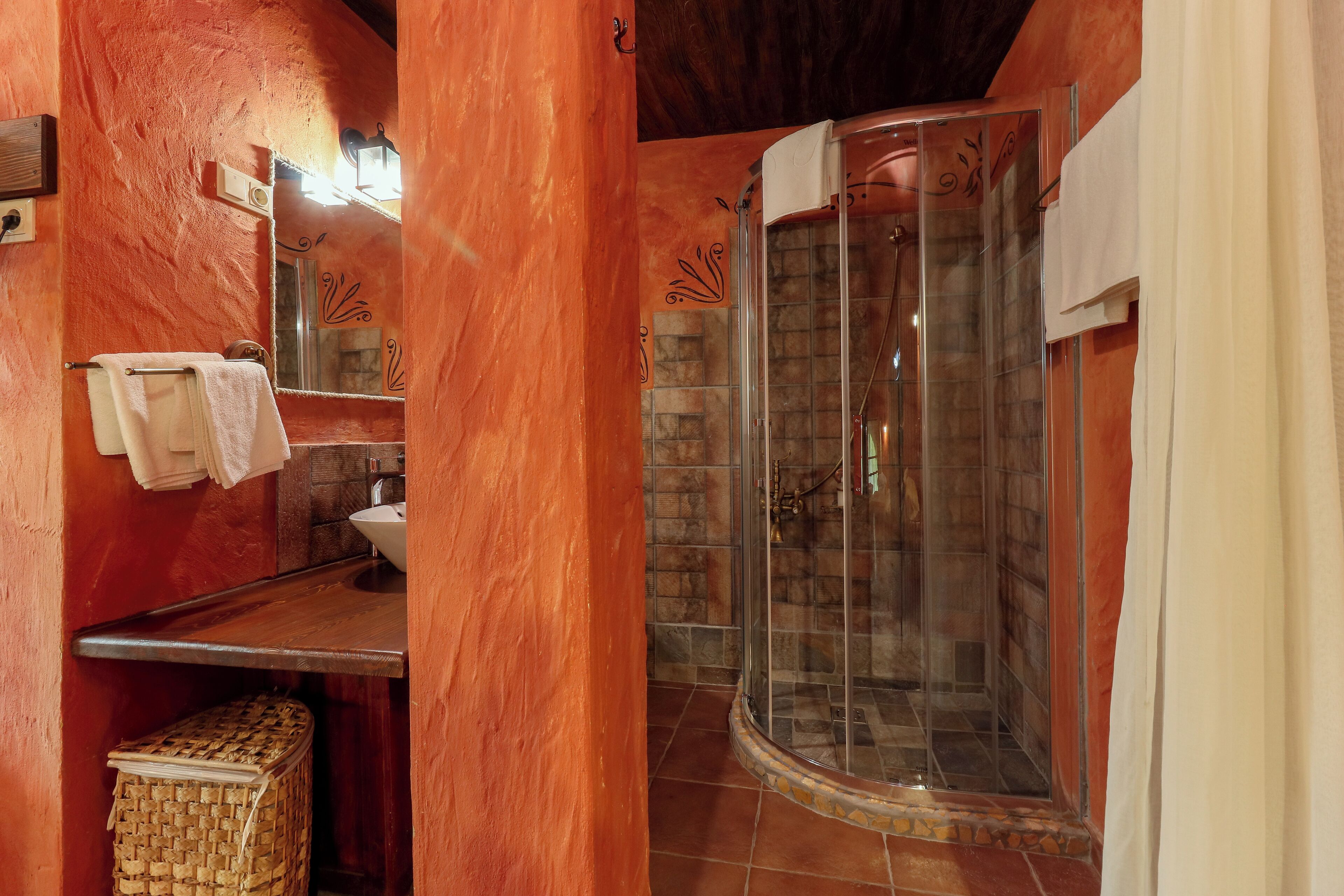 A bathroom with a stone wall, a glass shower enclosure, a wooden vanity, and a towel rack.