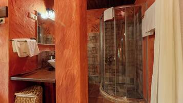A bathroom with a stone wall, a glass shower enclosure, a wooden vanity, and a towel rack.