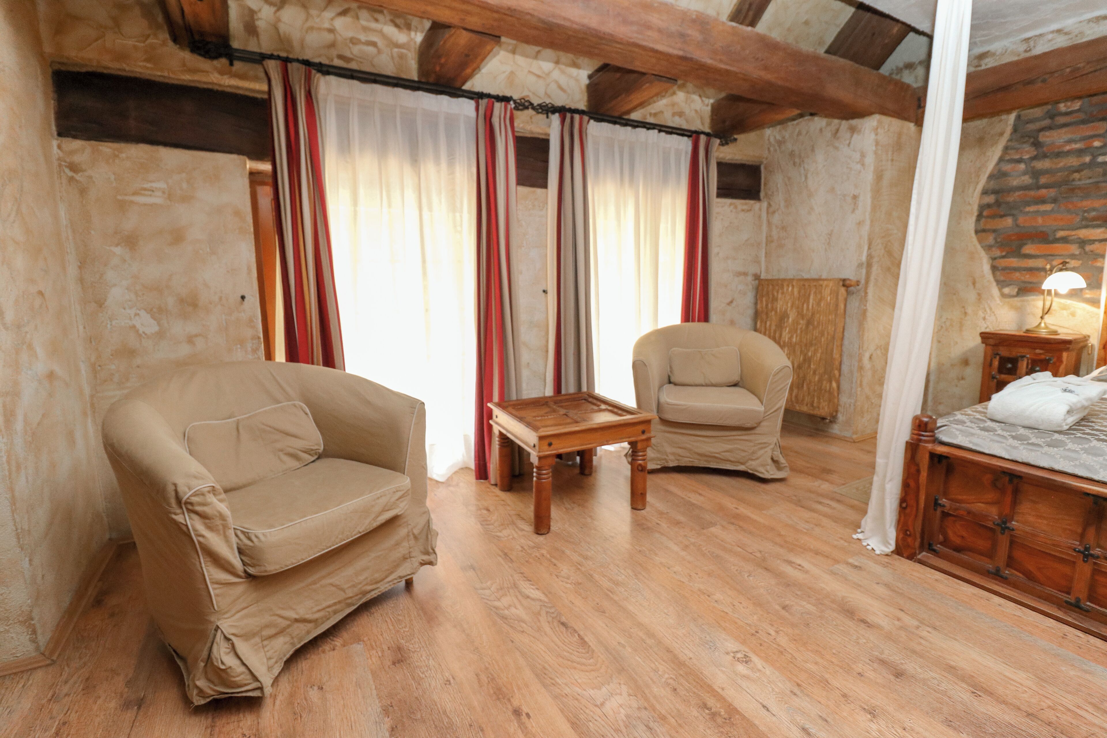 Una stanza accogliente con due poltrone beige, un piccolo tavolino in legno e un letto con testiera in legno.