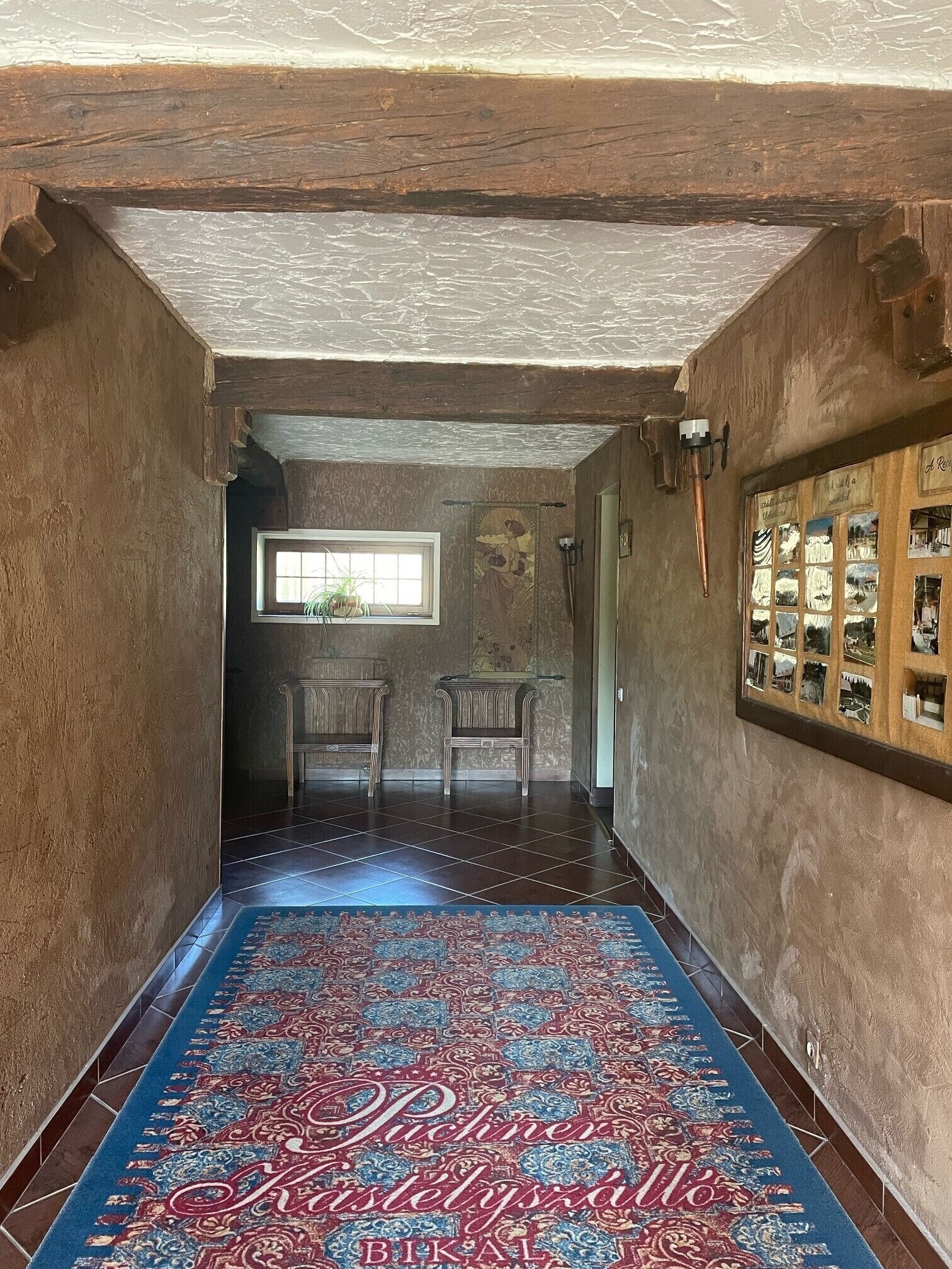 A narrow hallway with a patterned carpet, wooden walls, and a window with a plant.
