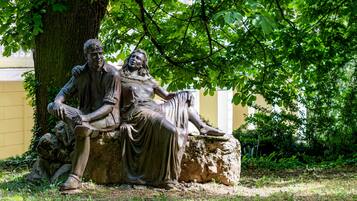A statue of two figures seated on a rock under a tree.