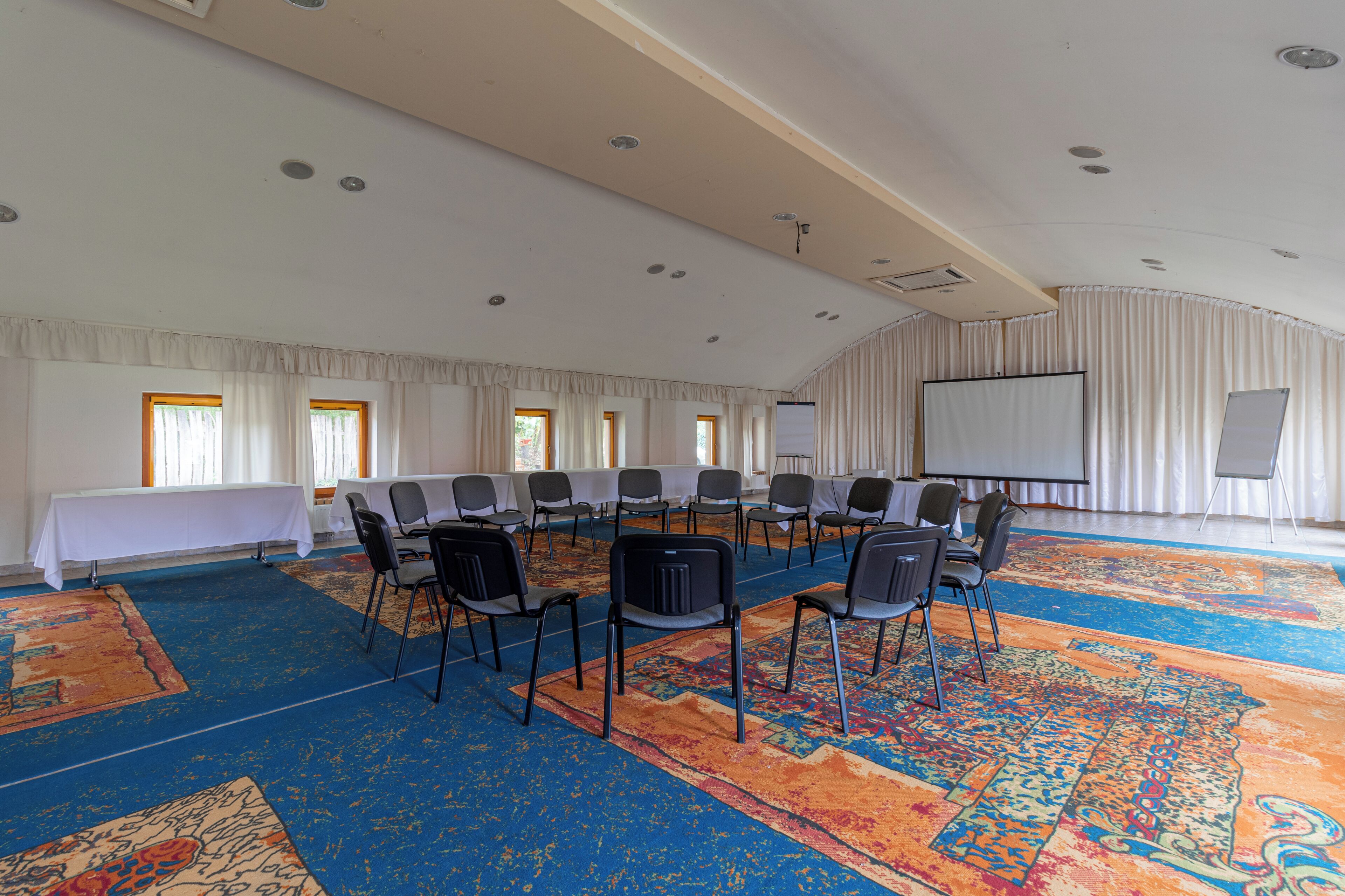 Un salón de conferencias con una larga mesa, sillas, una pantalla de proyector y una amplia alfombra.