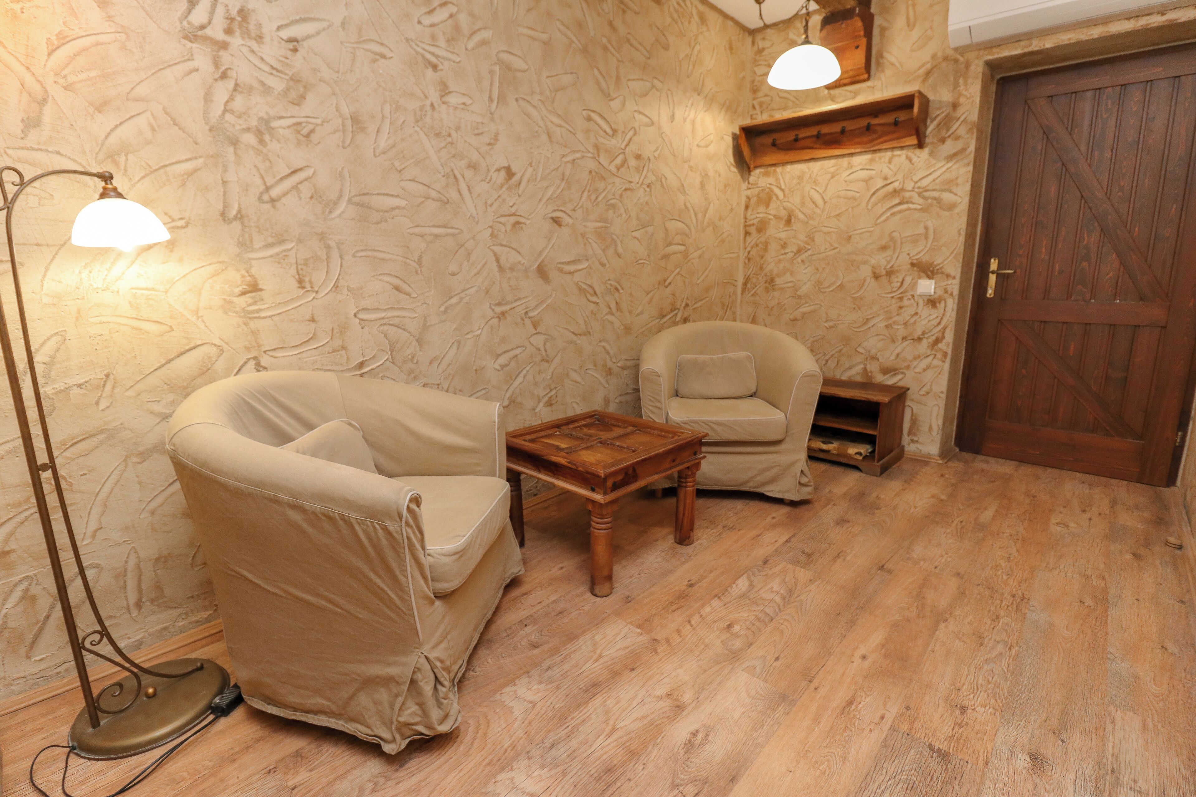 A room with a wooden floor, two beige armchairs, a small wooden table, and a wooden door.