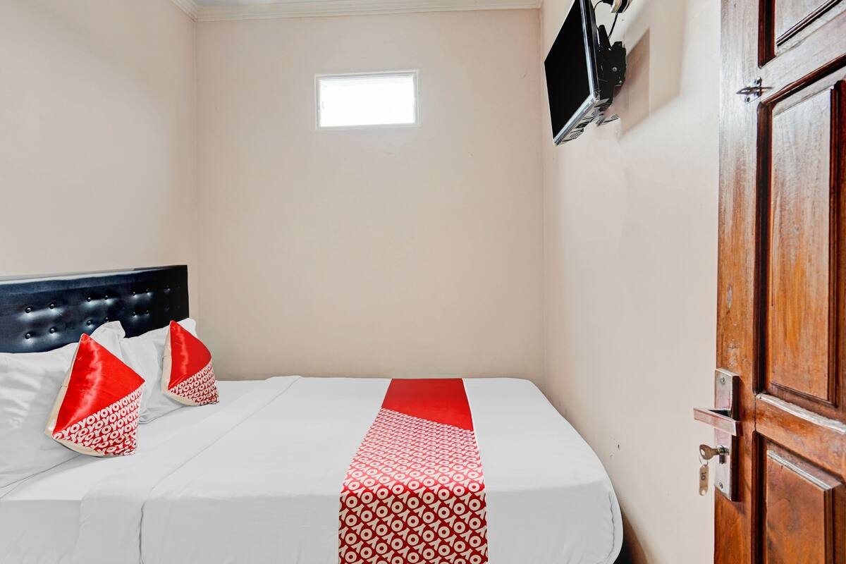 Una cama bien hecha con una corredora roja y blanca estampada, dos almohadas rojas y una pequeña ventana sobre la cama.
