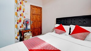 Een slaapkamer met een bed, een houten kledingkast, een ventilator en een gordijn met een bloemenprint.